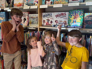 Four children posing in front of a bookshelf filled with various books.